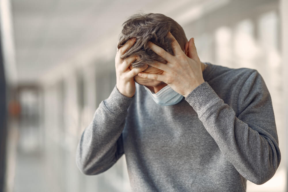 Un uomo indossa una mascherina e si tiene la testa, esprimendo ansia o disagio