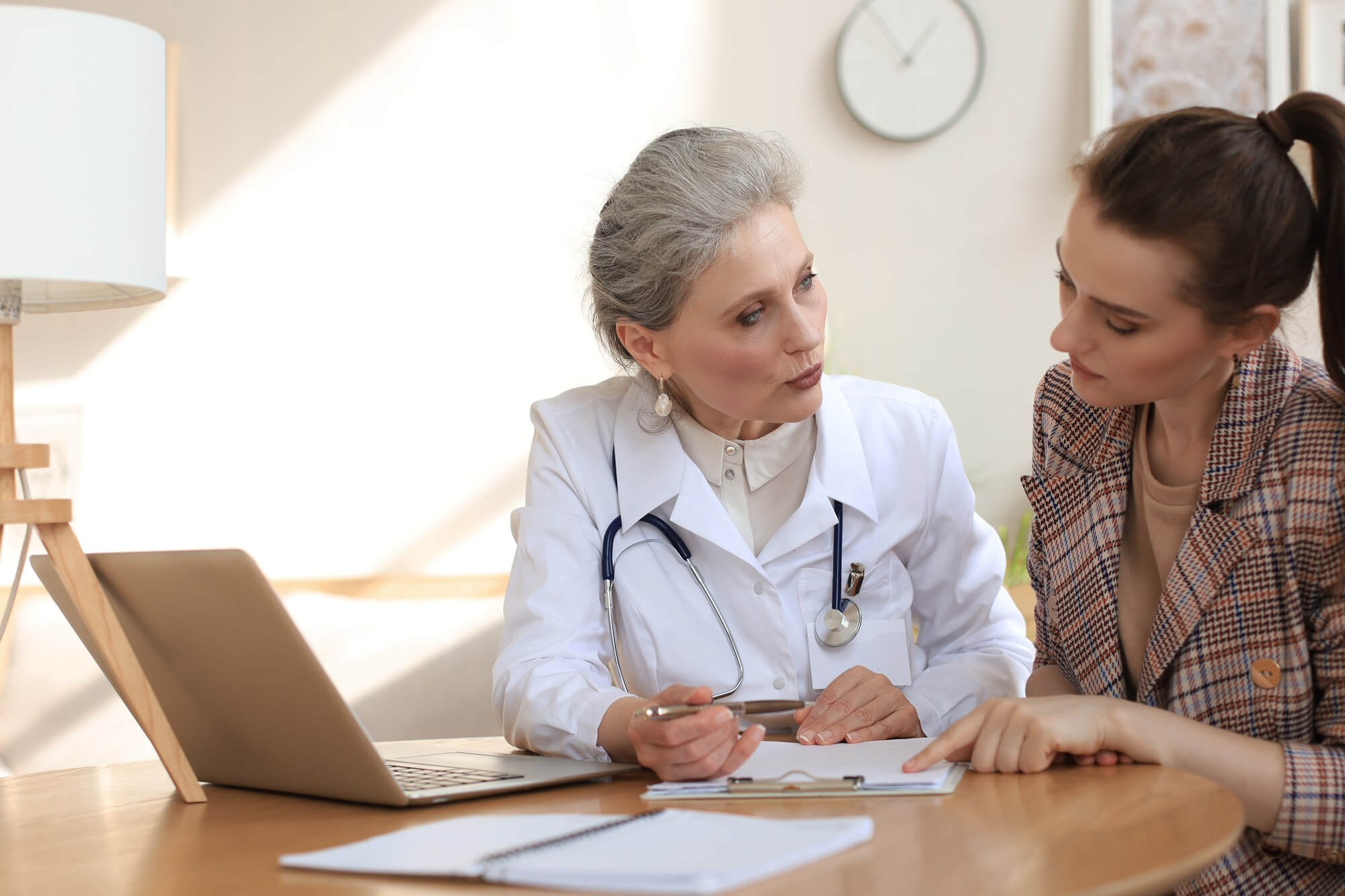 medico e paziente discutono su alcune analisi fatte dal paziente e sul tavolo sono appoggiati un computer e alcuni esami fatti