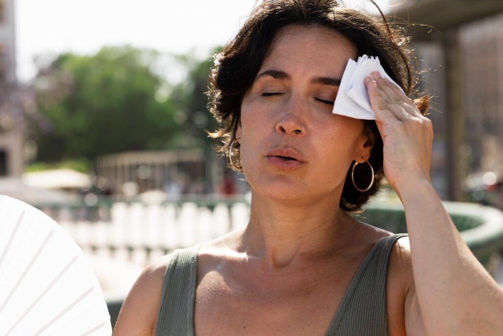 Una donna si fa aria con un ventaglio e si asciuga la fronte per il caldo
