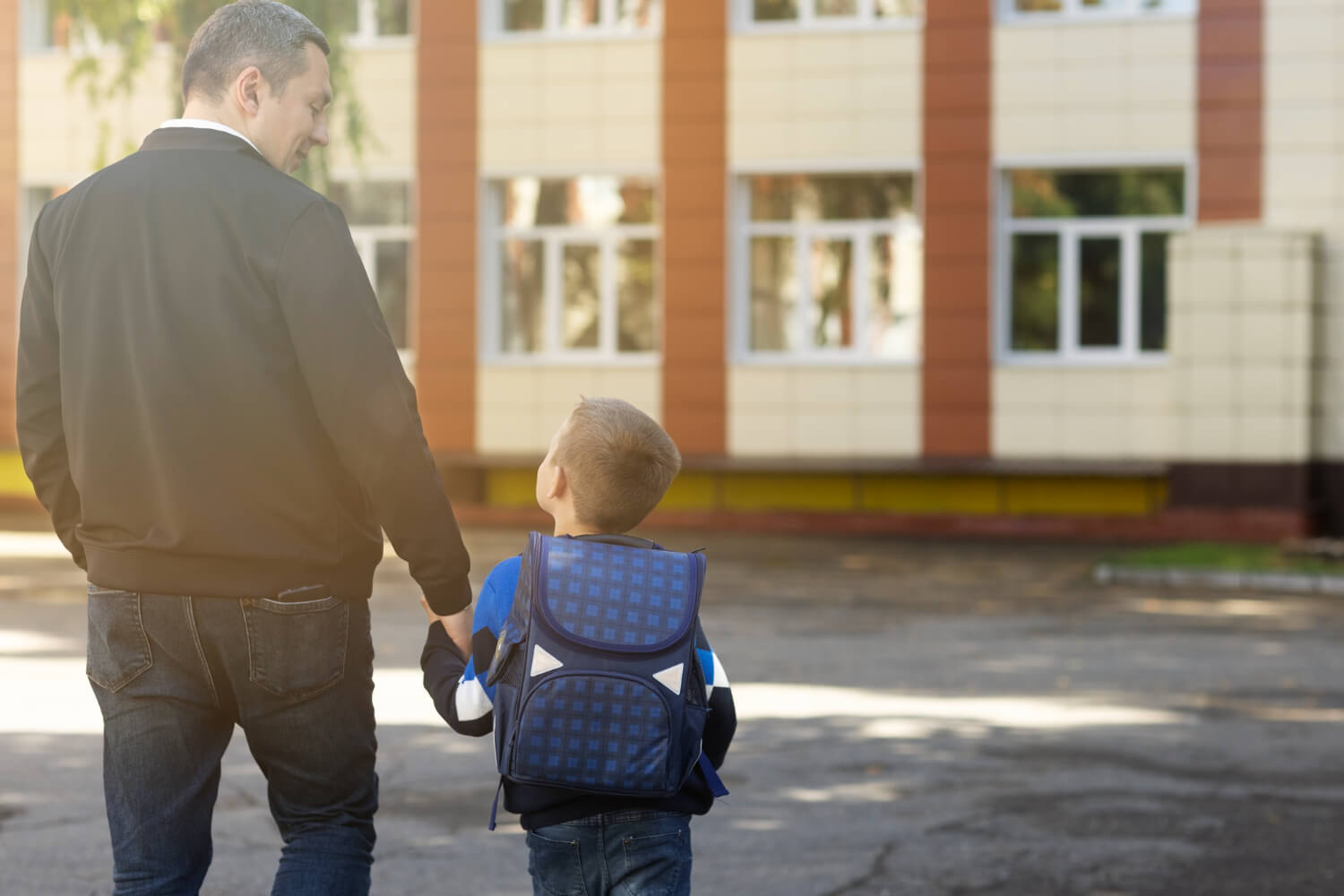 Un uomo dà la mano ad un bambino con uno zaino in spalla, accompagnandolo a scuola.