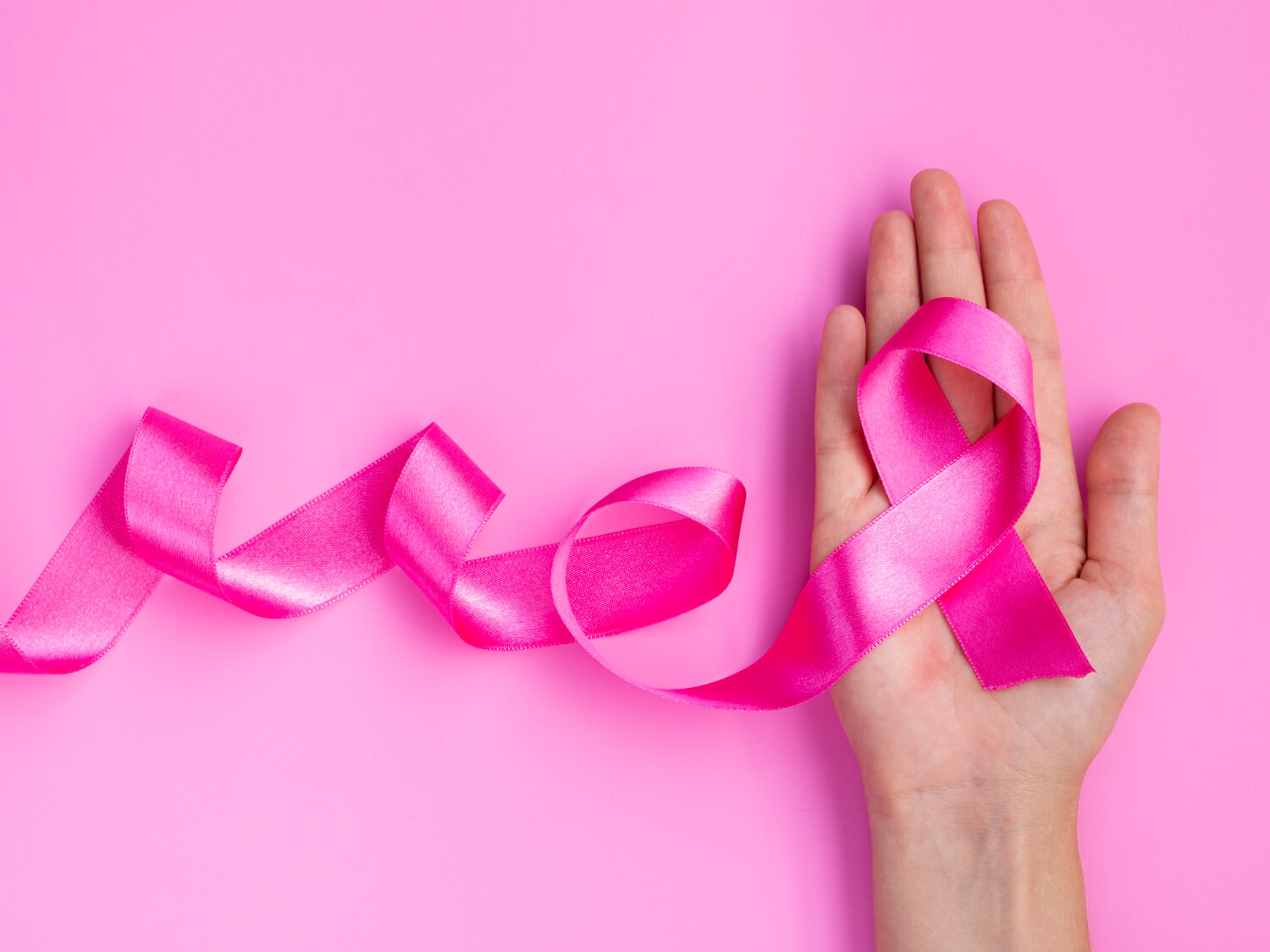 Mano con nastro rosa su sfondo rosa: simbolo della prevenzione del tumore al seno e della campagna Ottobre Rosa